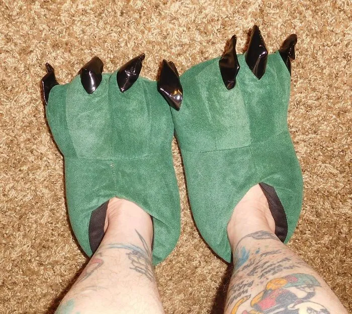 Green monster claw slippers on tattooed legs, adding humor to any outfit.