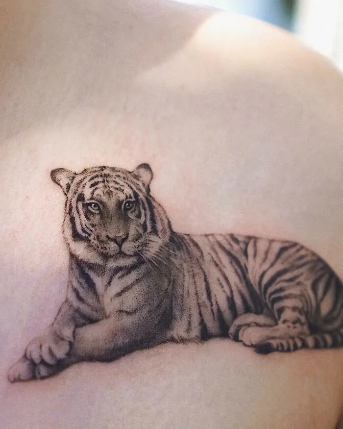 Tattoo of a lying tiger, showcasing painting-like detail with natural and animal elements by Korean ink artist.