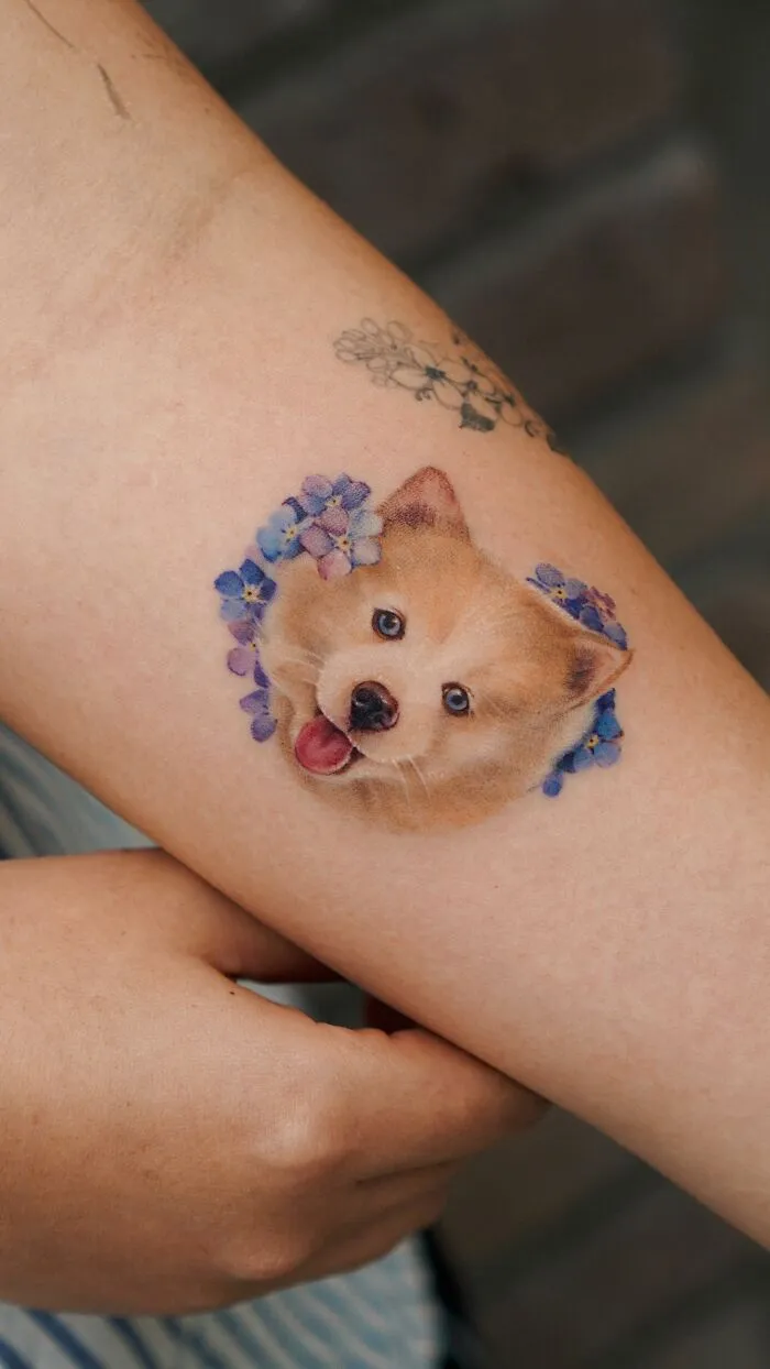 Painting-like tattoo of a dog's face with purple flowers, blending nature and animals on a person's arm.