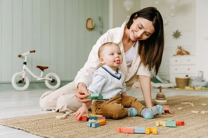 A mother playing with her baby on a rug with building blocks, showing family time and child development. Horrible resumes.