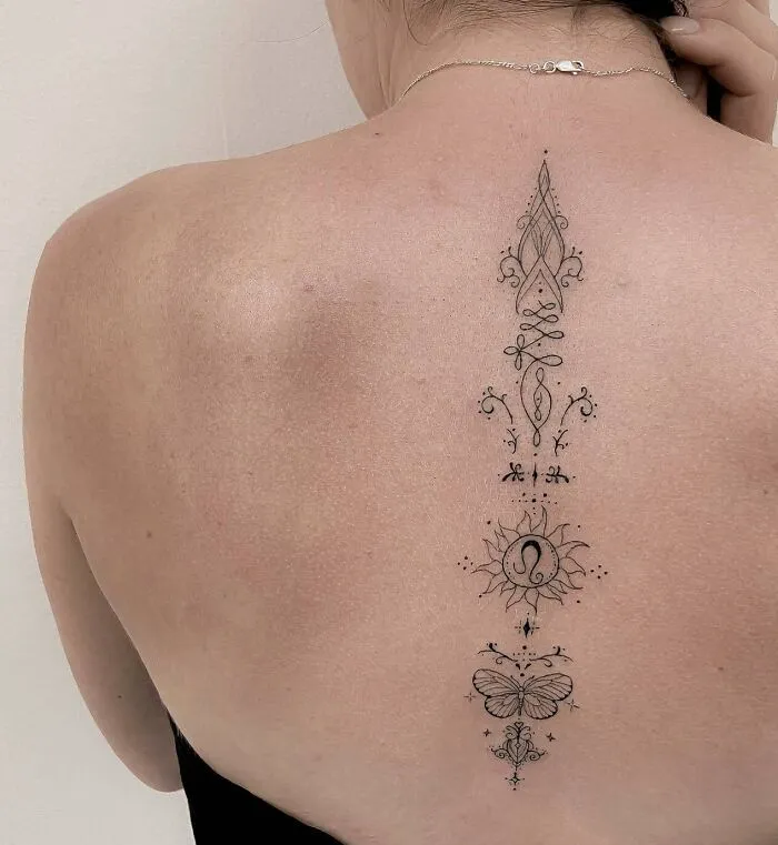 Intricate spine tattoo featuring delicate designs, including a sun and butterfly, on a person's back.