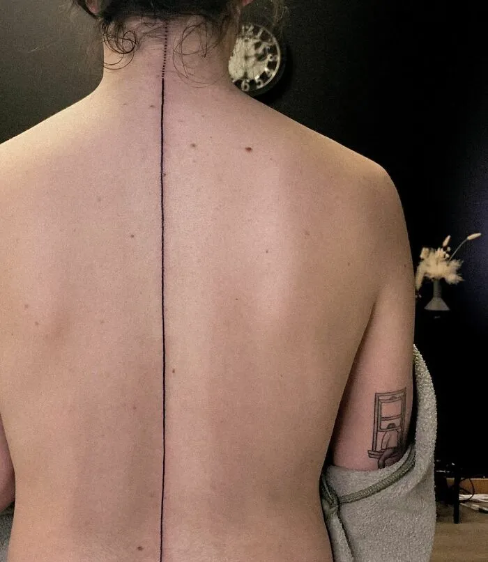 Bare back featuring a linear spine tattoo in a minimalist room.