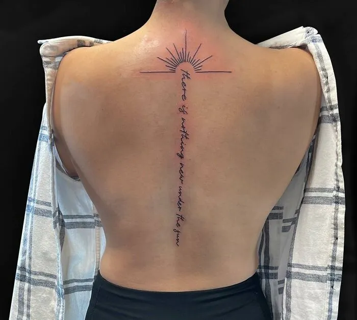 Tattoo featuring a sun and quote along the spine on a person's back.