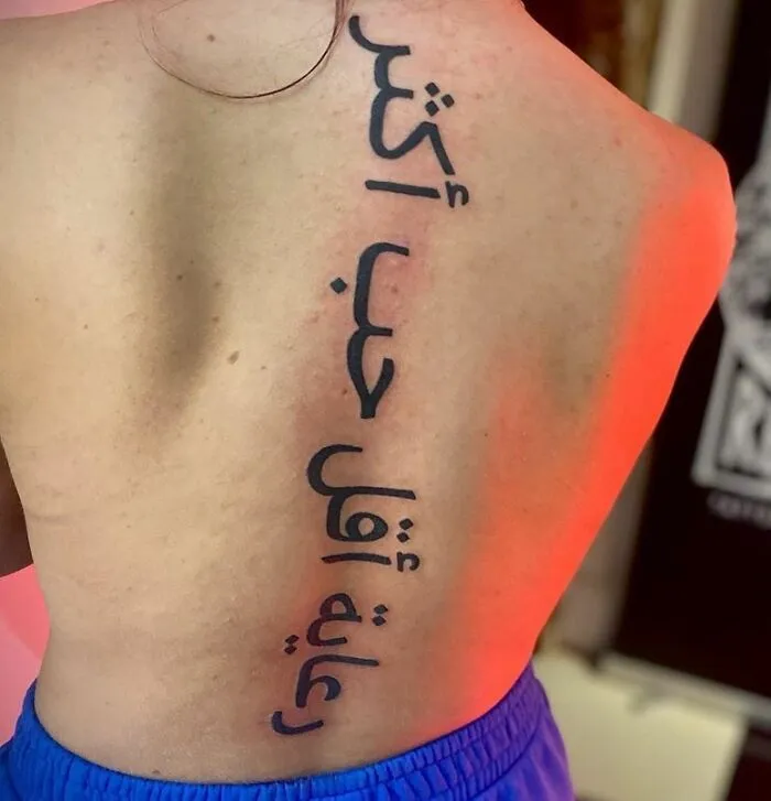 Arabic calligraphy tattoo on spine, beautifully aligned from neck to lower back.