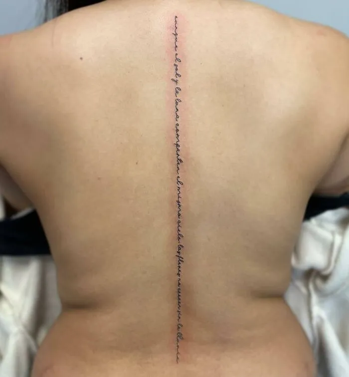 Elegant spine tattoo with script design down the center of the back.