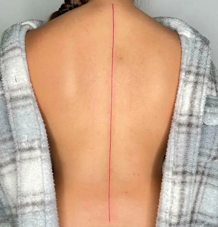 A minimalistic red line spine tattoo on a person's back, enhancing their natural beauty.