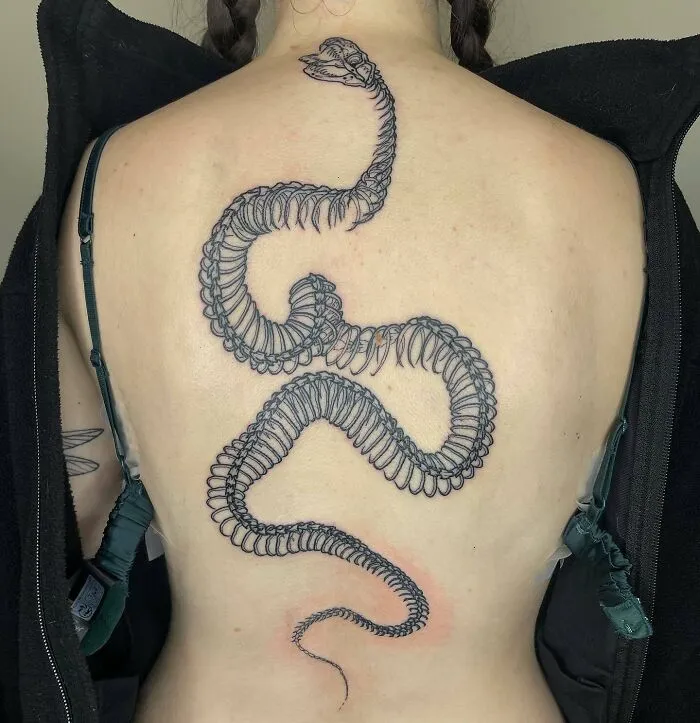 Snake skeleton spine tattoo on woman's back, showcasing beautiful spine tattoos.