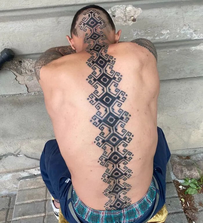 Geometric spine tattoo design running from neck to lower back on a seated person.
