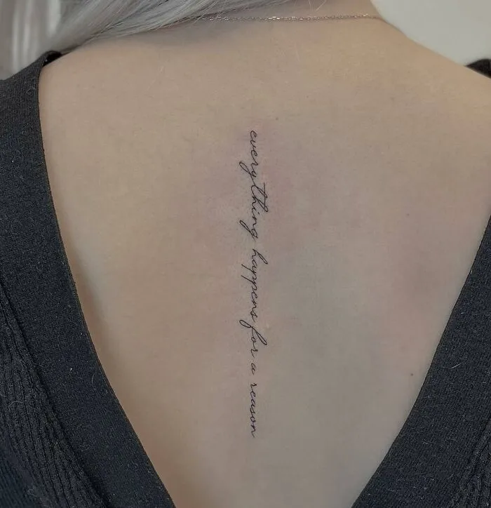 Script tattoo along the spine reading "everything happens for a reason," showcasing beautiful spine tattoo design.