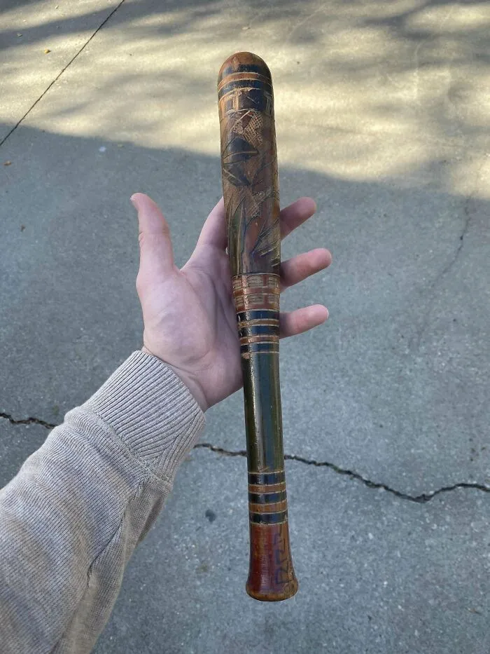 Antiguo objeto de madera parecido a un bate con tallas florales