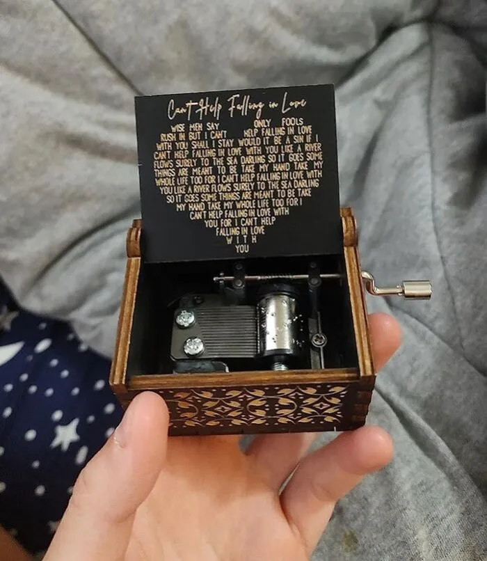 Hand holding a small wooden music box with intricate designs, perfect affordable Valentine's Day gift under $25.