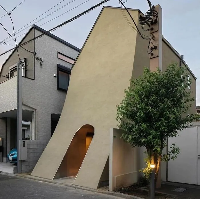 Unique architectural design of a narrow, triangular building next to two modern houses.
