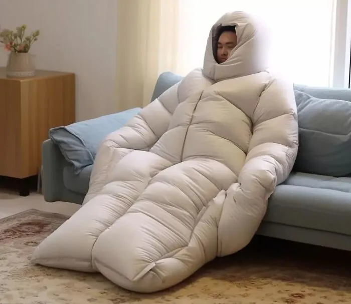 Person comfortably wrapped in a white, puffy design suit, seated on a couch in a cozy room.