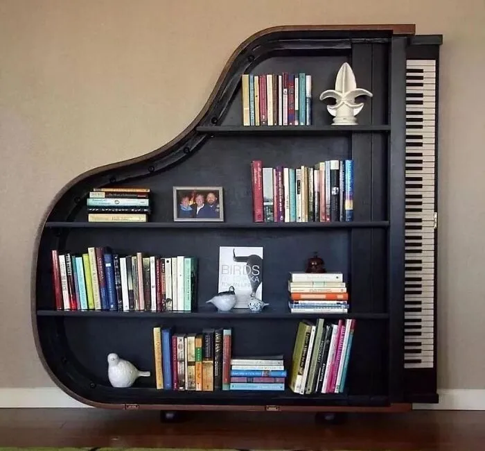A piano-shaped bookshelf filled with books and decorative items. Design and creativity blend seamlessly.