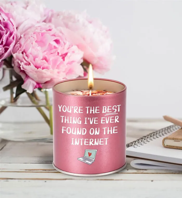 Affordable Valentine's Day gift candle with a humorous message, next to pink flowers and a notebook.