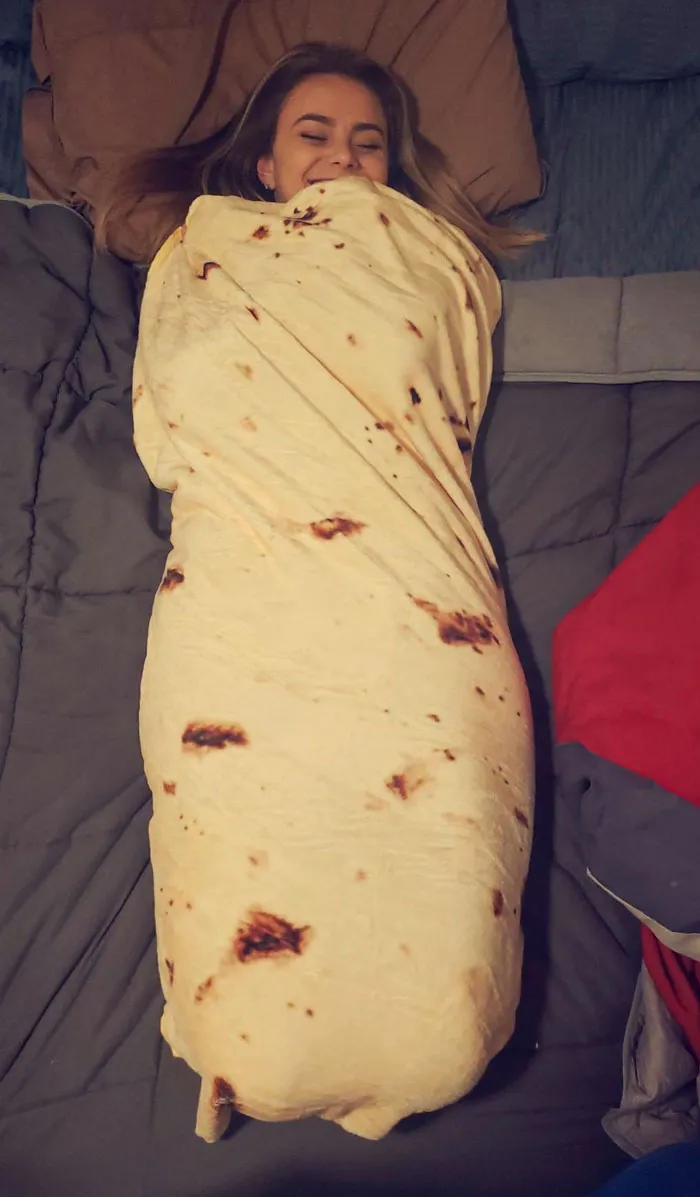 Person wrapped in a blanket resembling a tortilla, smiling while lying comfortably. Valentine's Day gifts idea.