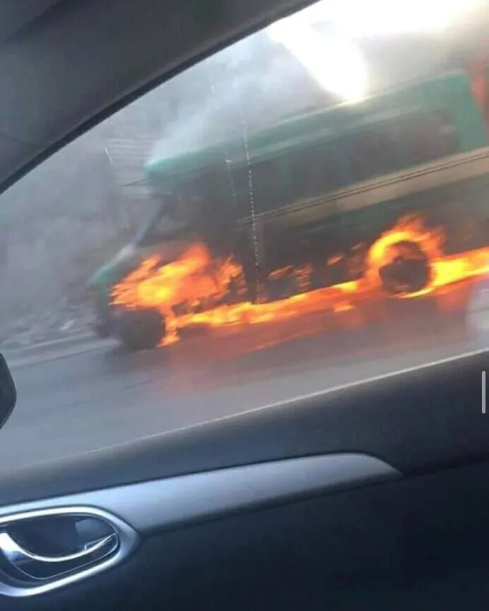 A bus on fire seen from a car window, creating a strange and cursed image.