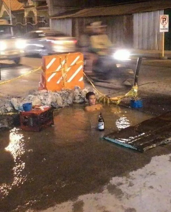 Man sitting in a makeshift pool on a street, surrounded by barriers, making the scene look weird.