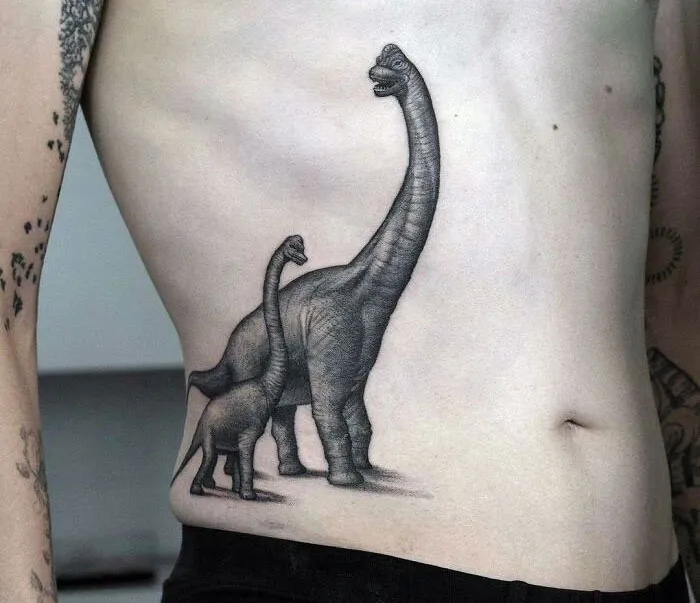 Detailed dinosaur tattoo on someone's side, showcasing two dinosaurs in black ink.