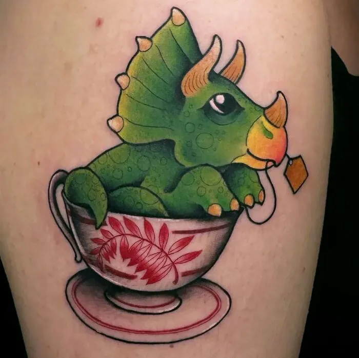 A green triceratops dinosaur tattoo in a teacup, showcasing a creative and whimsical design.