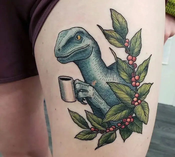 Dinosaur tattoo of a velociraptor with a coffee cup, surrounded by leafy branches with red berries on a leg.