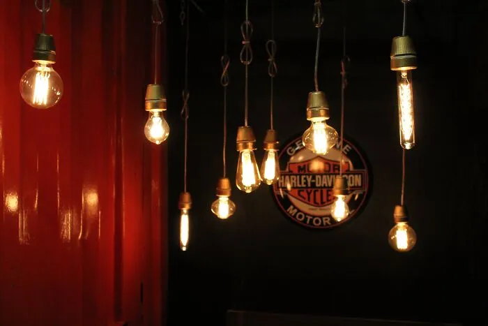 Hanging Edison bulbs, symbolizing a failed innovation concept, glow dimly by a red wall and Harley-Davidson sign.
