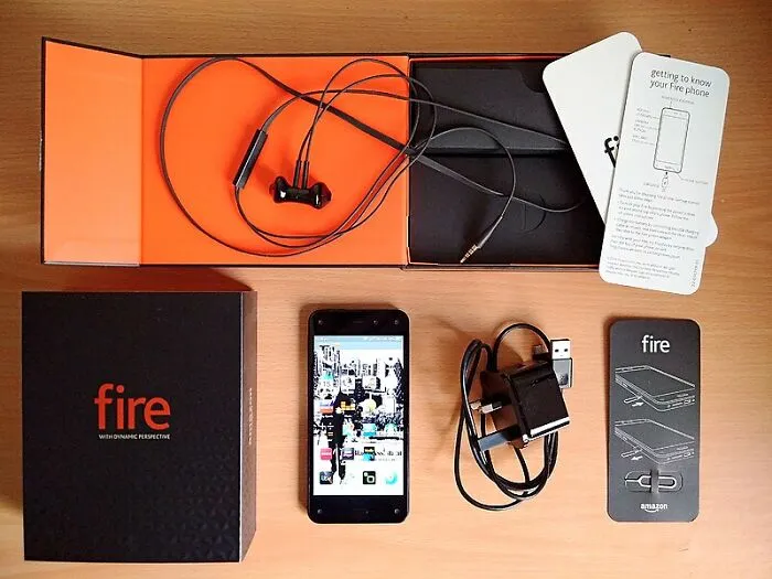 Amazon Fire Phone with accessories, once hyped as the next big thing in smartphones, displayed on a wooden surface.