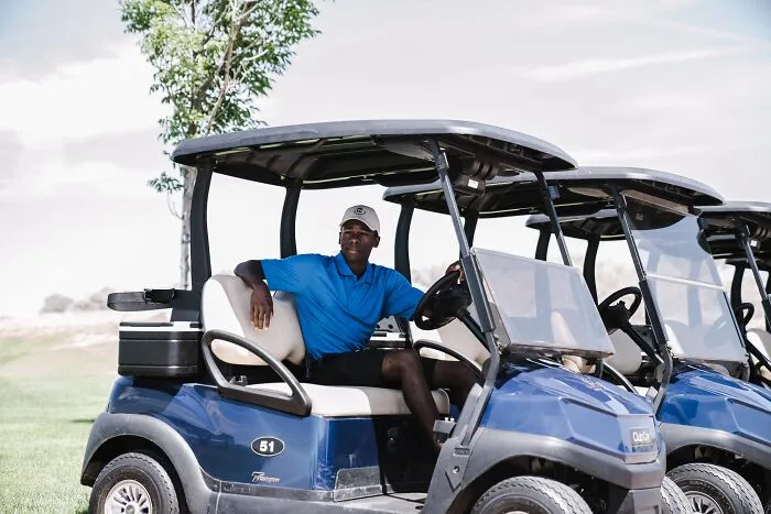 A person sitting in a blue golf cart on a grassy course, trying advice from a tutorial.