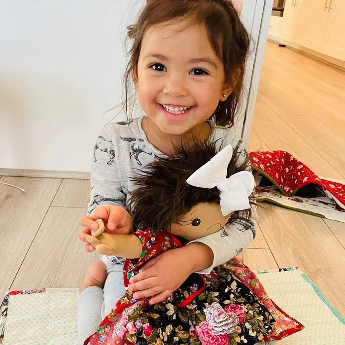 A girl with health conditions, smiling and holding her inclusive doll.