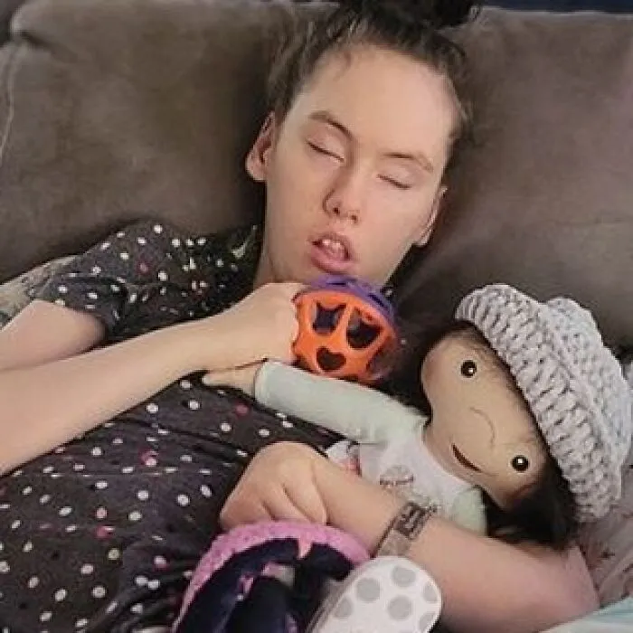 A girl with her eyes closed, embracing an inclusive doll with health conditions.