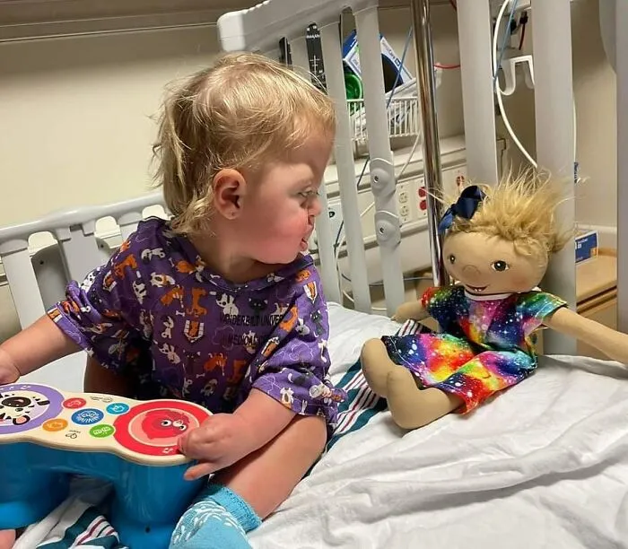 A toddler in a hospital bed with an inclusive doll matching her, representing health conditions.