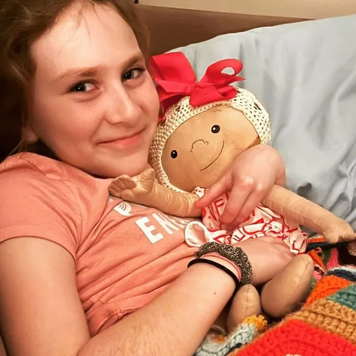 A young girl happily cuddles her inclusive doll, designed to represent her health conditions.