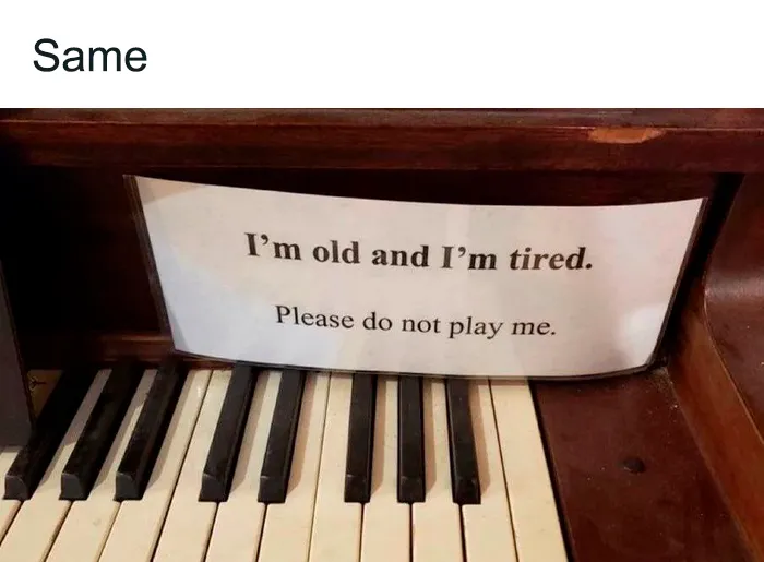 Piano with a sign reading "I'm old and I'm tired," a relatable mental health meme humorously expressing fatigue.