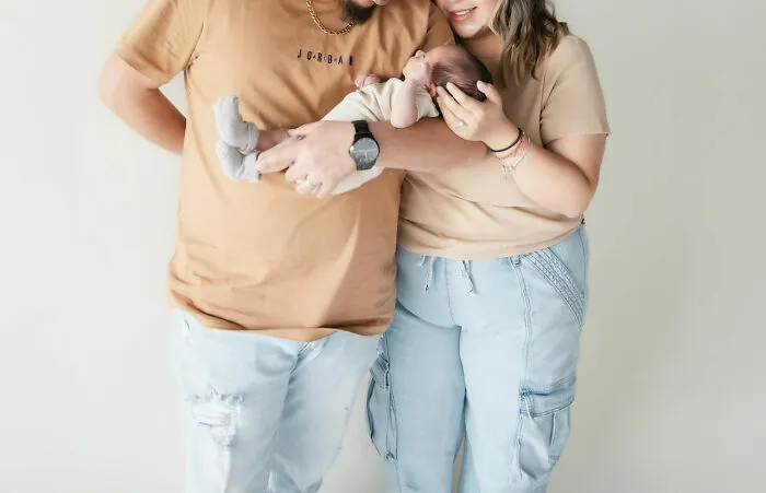 Couple in matching outfits lovingly hold their baby, highlighting unique baby names trend.