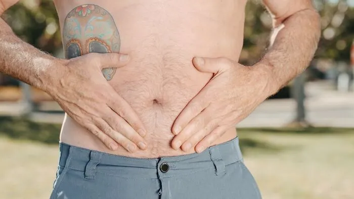 Shirtless man with tattoo, hands on stomach.