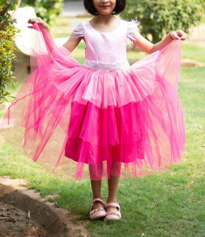 A young girl outdoors in a pink dress holding its sides, showing off an unfortunate yet humorous style choice.