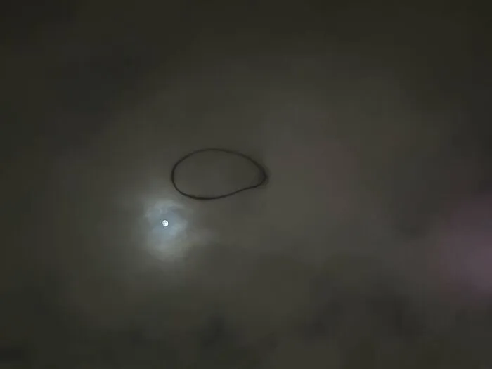 Oddly terrifying circle shape in the night sky with the moon visible through clouds.