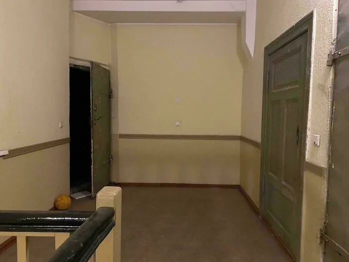 Dimly lit eerie hallway with green doors, open entrance, and a basketball, creating an oddly terrifying scene.