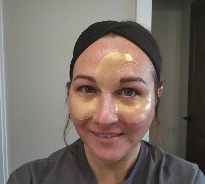 Woman smiling with under-eye and forehead gold patches, a cheerful and cheap Mother's Day gift idea.