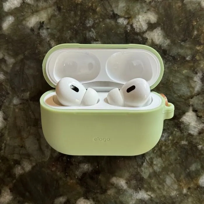 Wireless earbuds in a green protective case on a dark granite surface, essential for travel summer itinerary accessories.