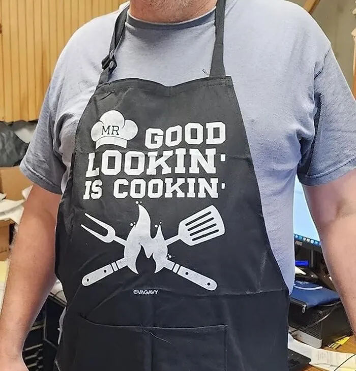 A man wearing an apron that says Mr Good Lookin is Cookin, a fun last minute Father's Day gift.