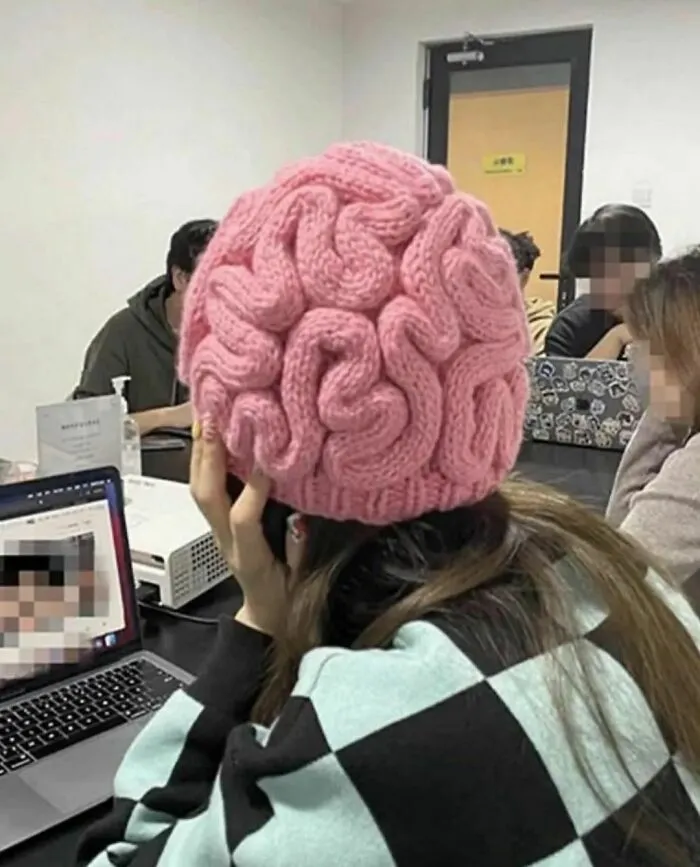 Persona con gorro tejido en forma de cerebro en reunión, imagen curiosa y divertida que puede resultar incómoda.