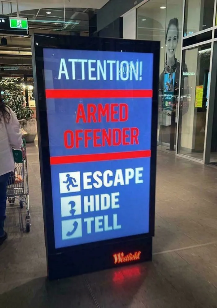 Sign in a mall warning about armed offender with instructions to escape, hide, and tell; oddly terrifying atmosphere.