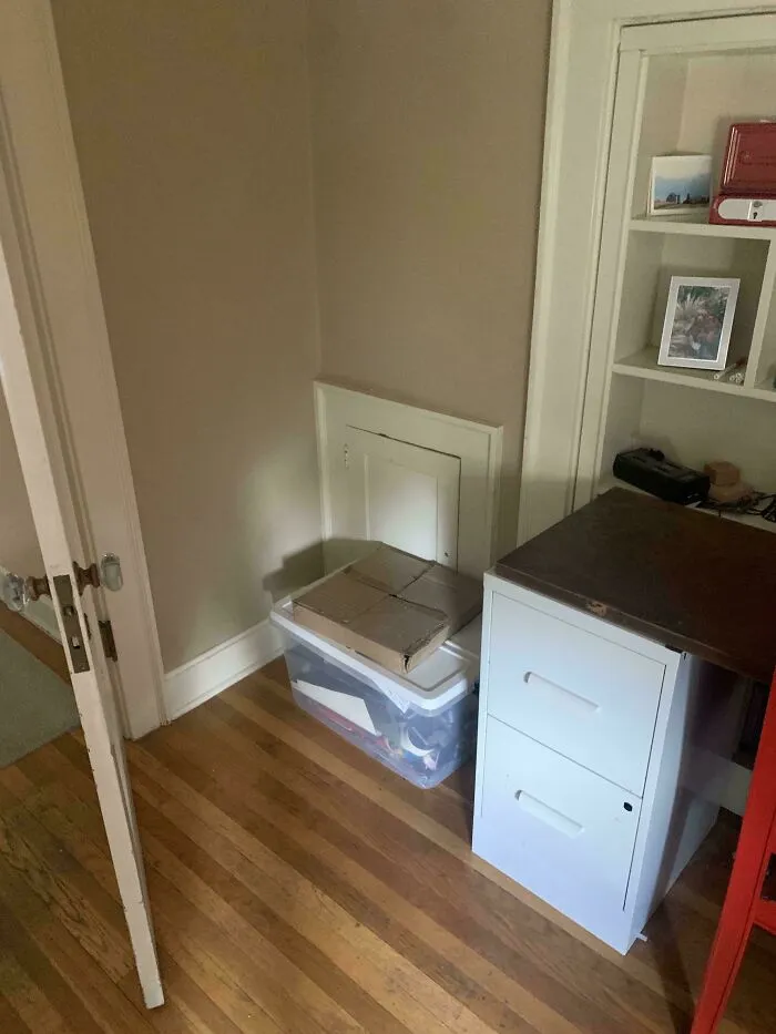 Oddly terrifying hidden door with a mysterious vibe, next to storage bins and a filing cabinet in a dim corner.