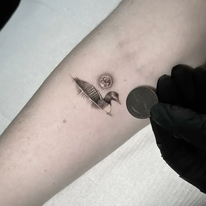 Single needle tattoo of a bird next to a coin on pale skin, showcasing detailed artistry.