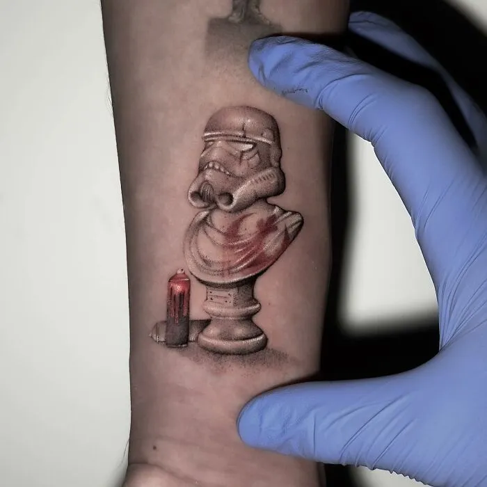 Single needle tattoo of a stormtrooper bust and red candle on an arm, with a gloved hand revealing the art.