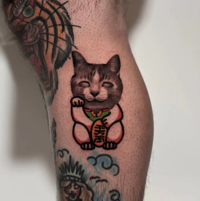 Tattoo combining traditional and photorealistic styles, depicting a cat with elements of a lucky cat design.