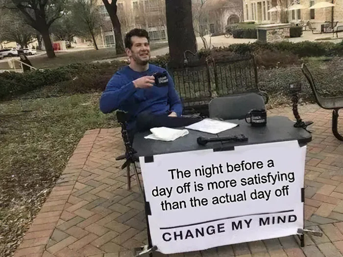 Man at a table with a sign about the night before a day off, sipping coffee outdoors. Happy Friday meme setting.
