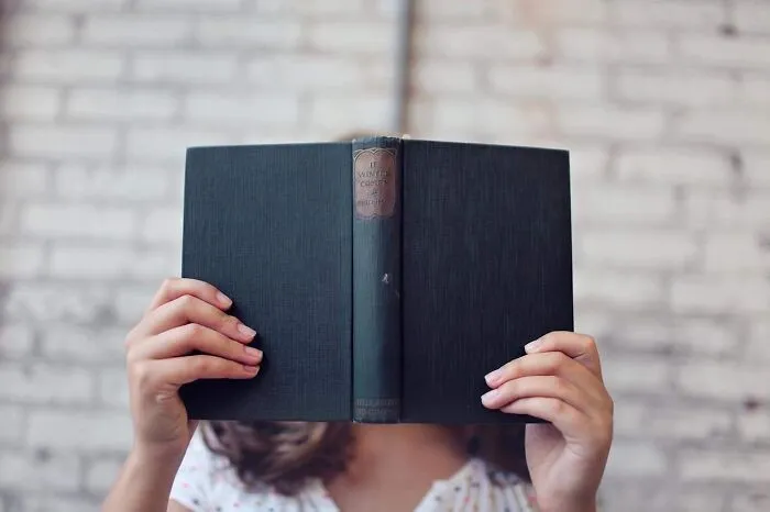 Person holding a book in front of a brick wall, embodying dad humor style.