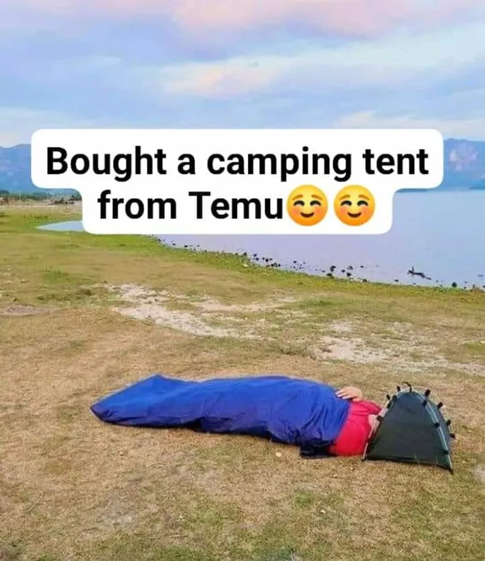 Person humorously using a small camping tent near a lake, referencing a funny Facebook post.